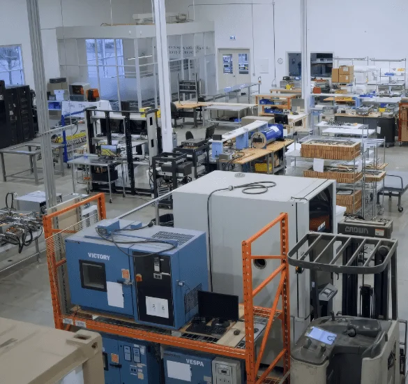 A high-angle view of a bright industrial laboratory or testing facility filled with various workstations, electronic testing equipment, and large blue machinery.